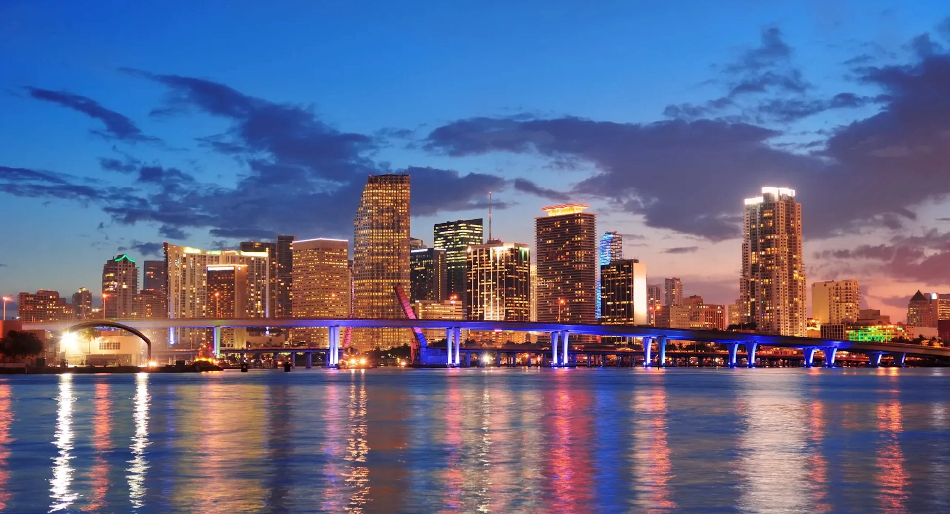 Miami skyline at dusk with illuminated buildings reflecting on Biscayne Bay water